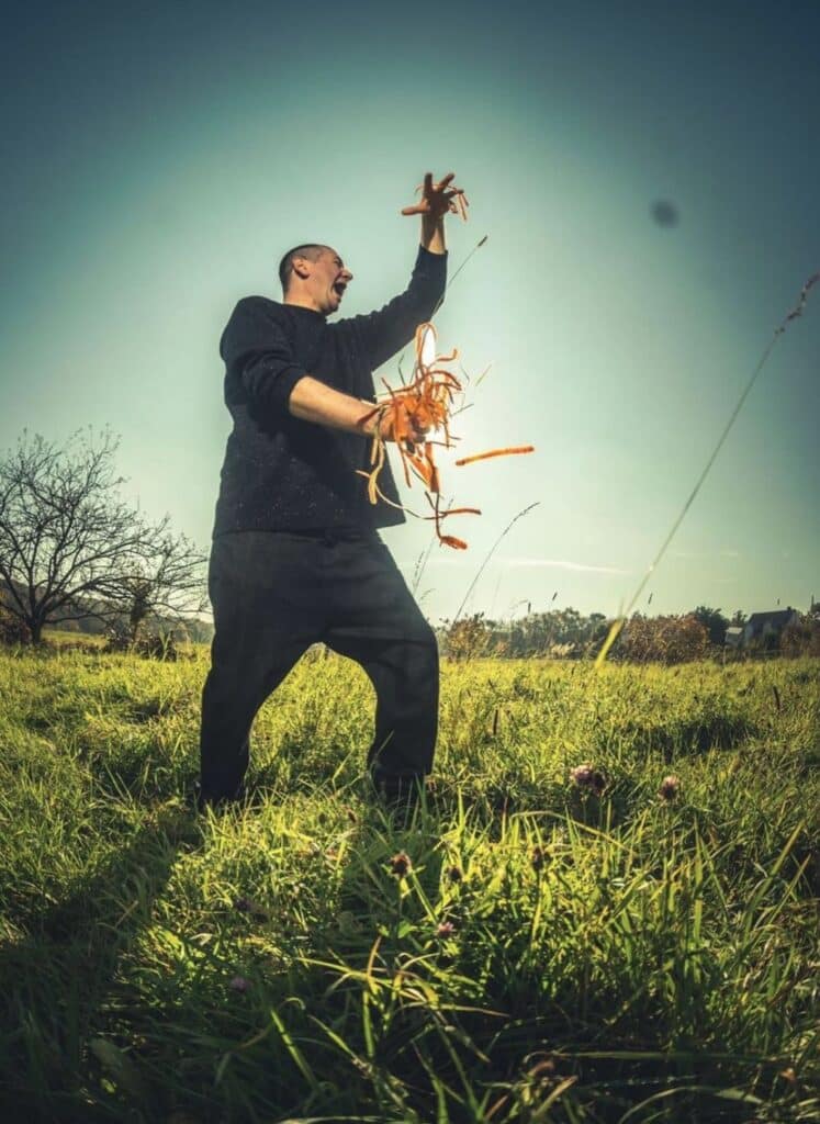 Der Koch CrissCasperGross steht auf auf einer Wiese mit Pflanzen in den Händen.